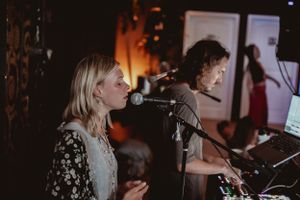 Musicians perform on stage at a dimly lit venue with microphones and instruments.