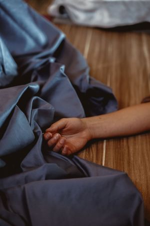Close-up of hand resting on blue fabric material on wooden surface.