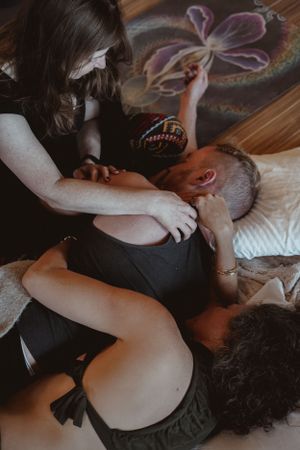 A massage therapy session takes place under artwork of a purple flower on wooden flooring.