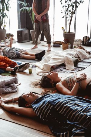 Participants lying in savasana pose during yoga class with plants in background.