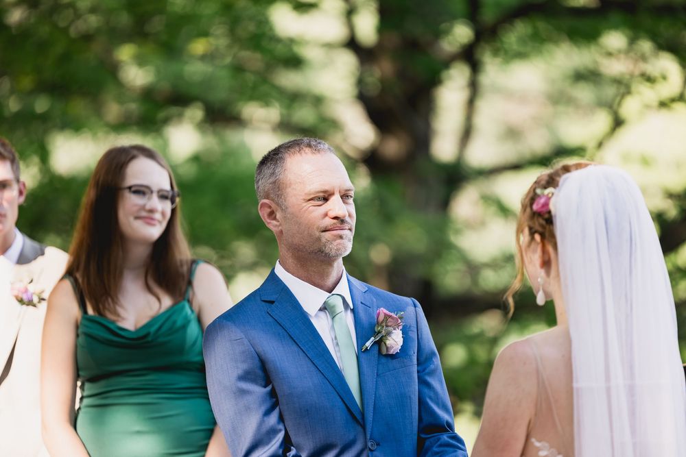 Wedding party poses together on a sunny day wearing coordinated emerald green dresses and navy blue suits.