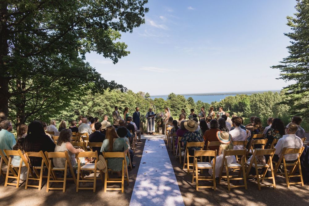 Outdoor wedding ceremony setup with wooden chairs and mountain vista through tree-lined clearing.