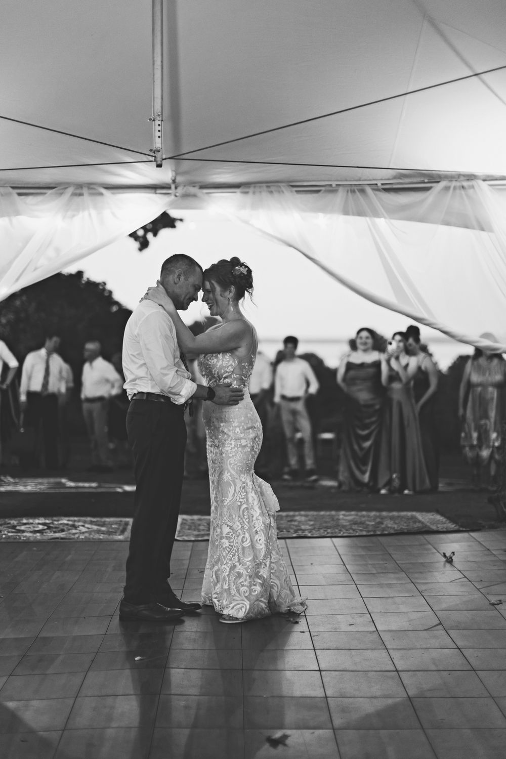 A couple shares their first dance under a white tent at their wedding reception.