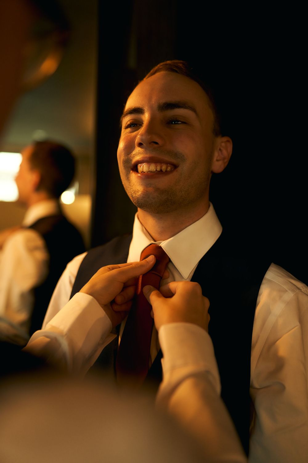 A warm moment captured as someone helps adjust a red tie during wedding preparations.