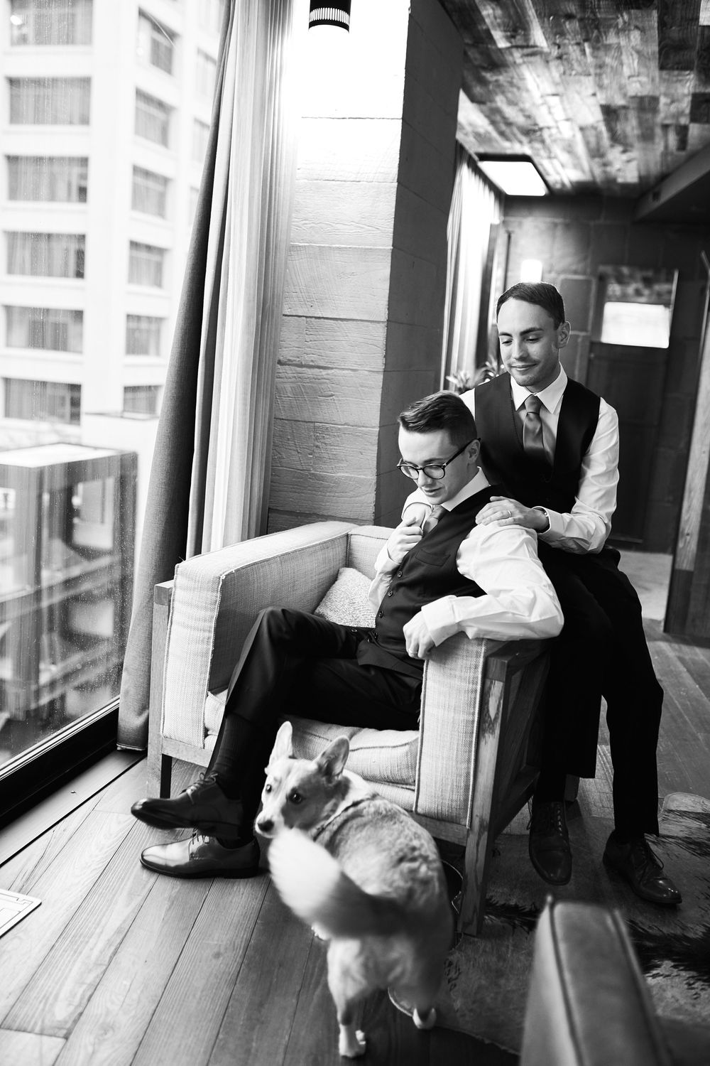 Formal-dressed figures relax by large windows in black and white photography.