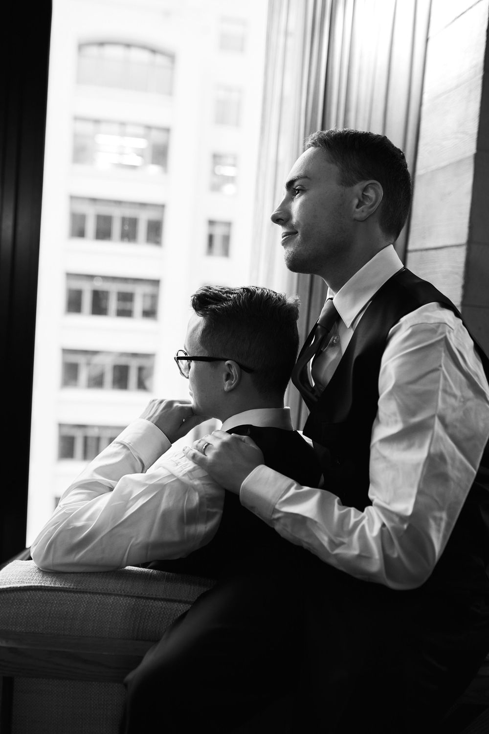 People in formal wear rest against window ledge in black and white photograph.