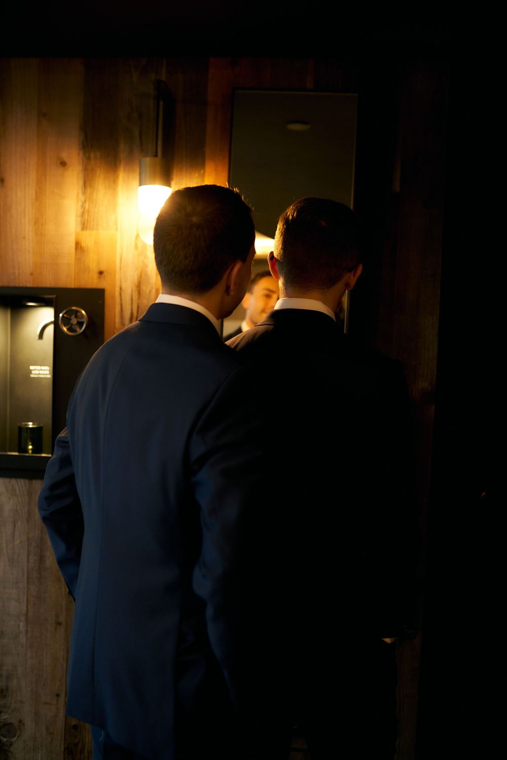 Shadowy figures in formal attire stand in dimly lit hallway.