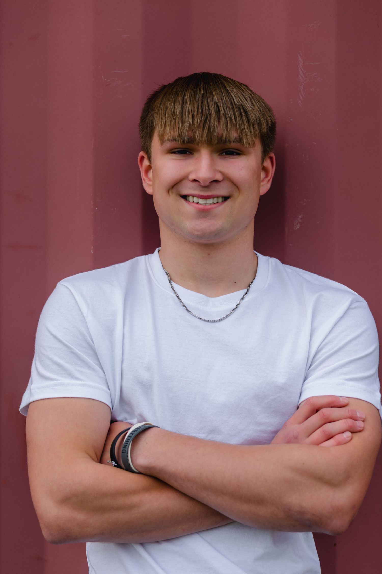 A person wearing a white t-shirt poses against a burgundy wall with crossed arms, shown at five different angles.
