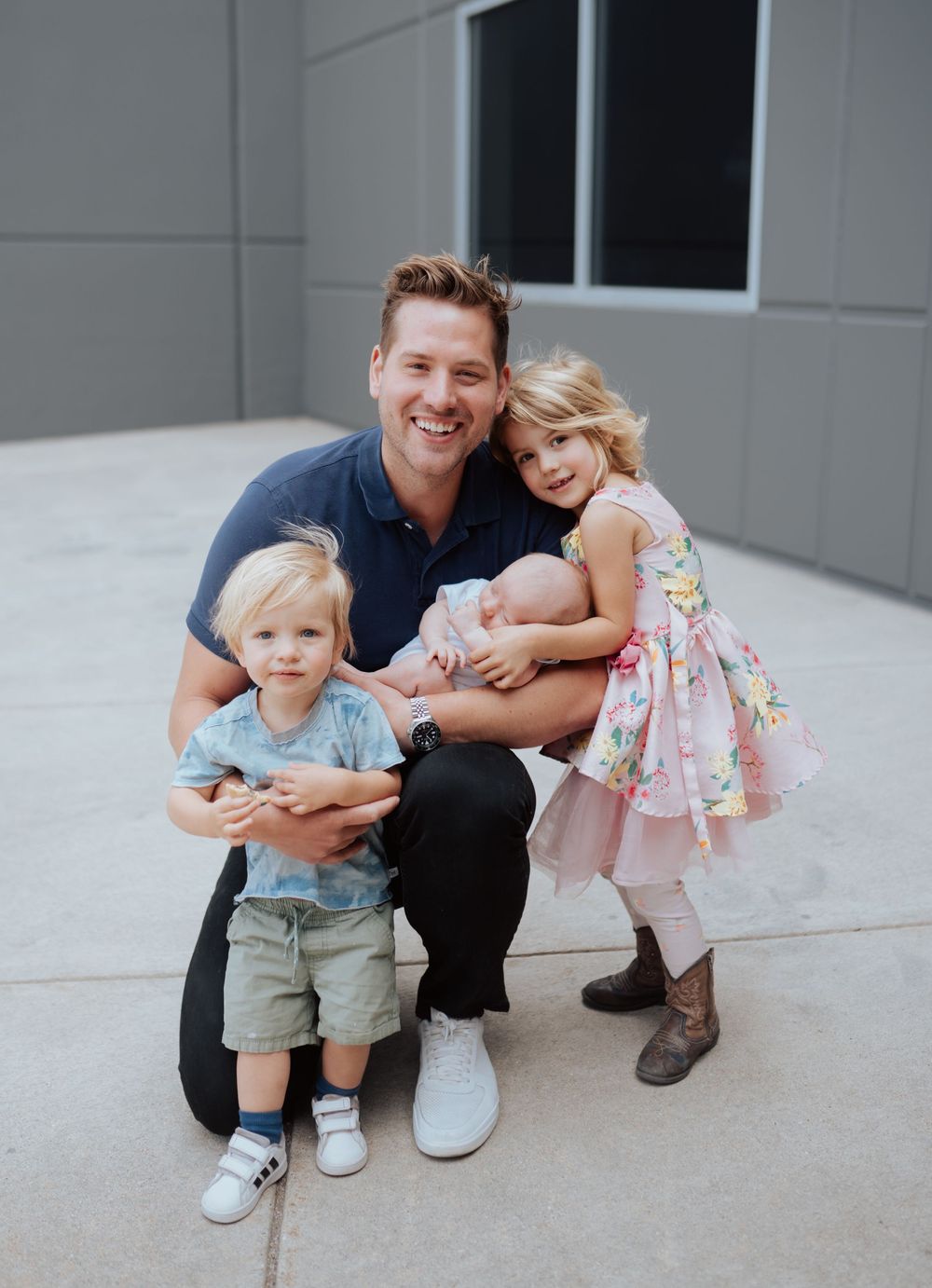 A parent and children pose together in a series of casual outdoor shots against a light colored wall.