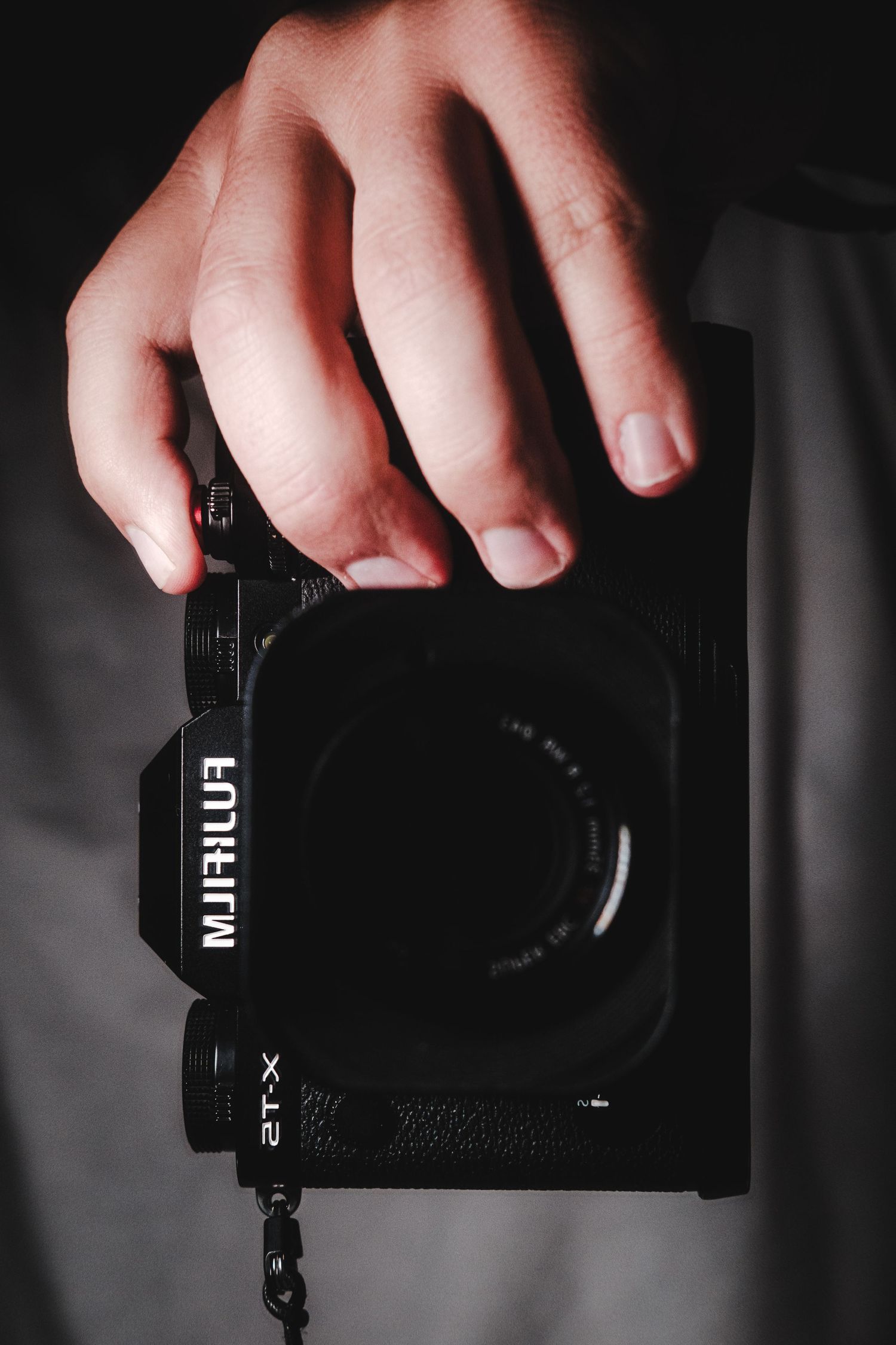A hand holds a black Fujifilm X-series camera against a dark background in selective color photography.