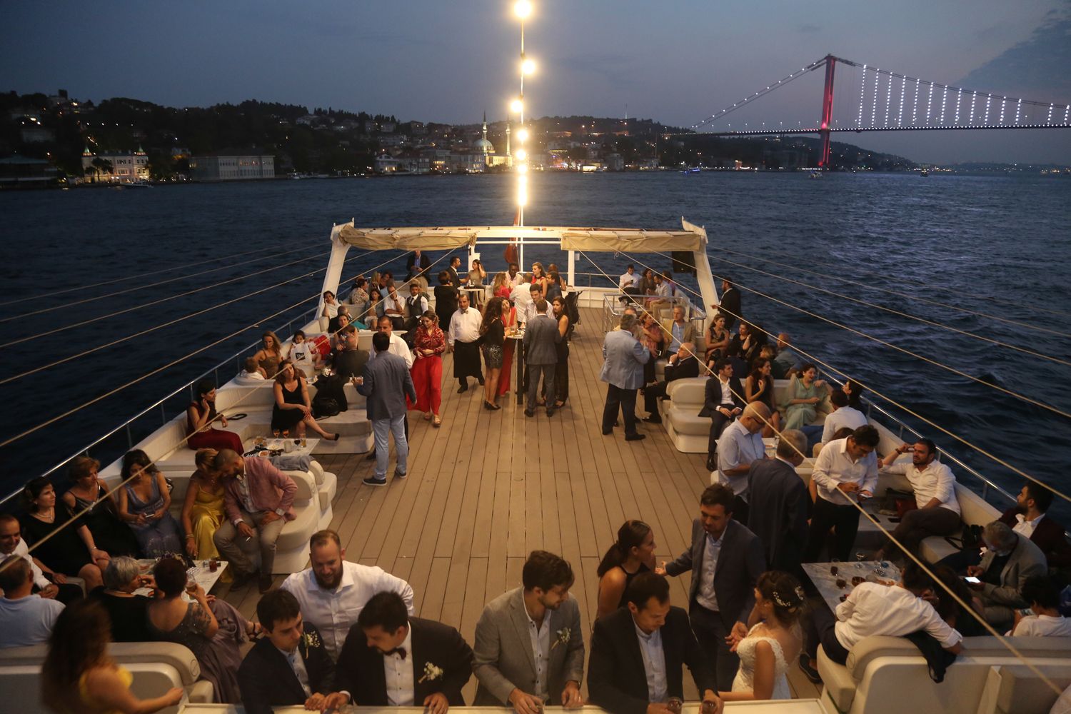 Party guests enjoying an evening boat cruise on the Bosphorus with the illuminated bridge visible in the background.