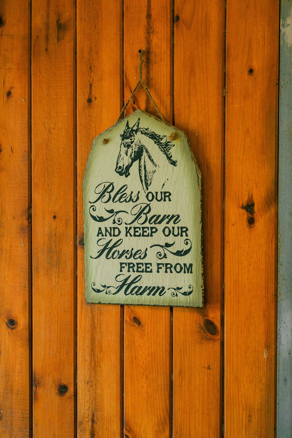 Rustic wooden sign with equestrian blessing text reading 'Bless our barn and keep our horses free from harm'.