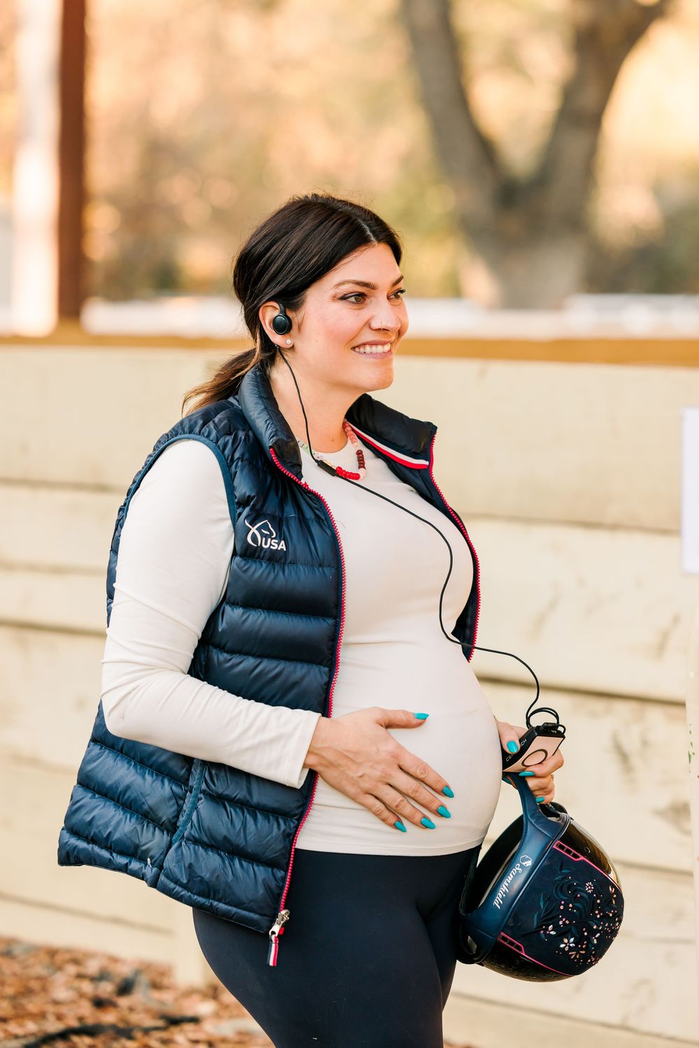 A person in a navy puffer vest holds a tumbler and bag while walking outdoors during winter.