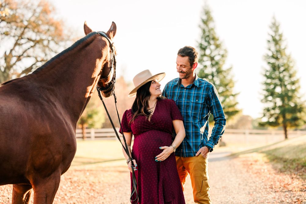 A couple poses with their chestnut horse during a sunset photo session in an outdoor field.