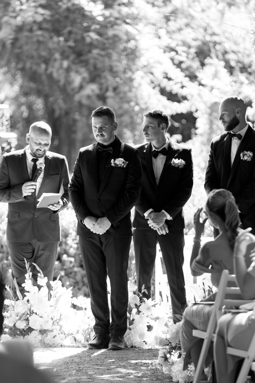 Groomsmen lined up outdoors in suits during wedding ceremony.