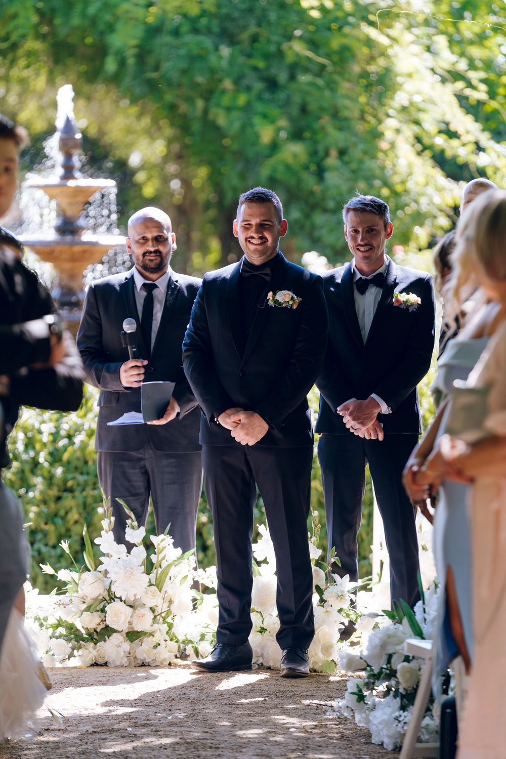 Wedding party in formal attire standing in a garden setting.