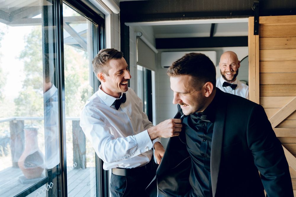 Groomsmen help adjust the bow tie and suit before the wedding ceremony.