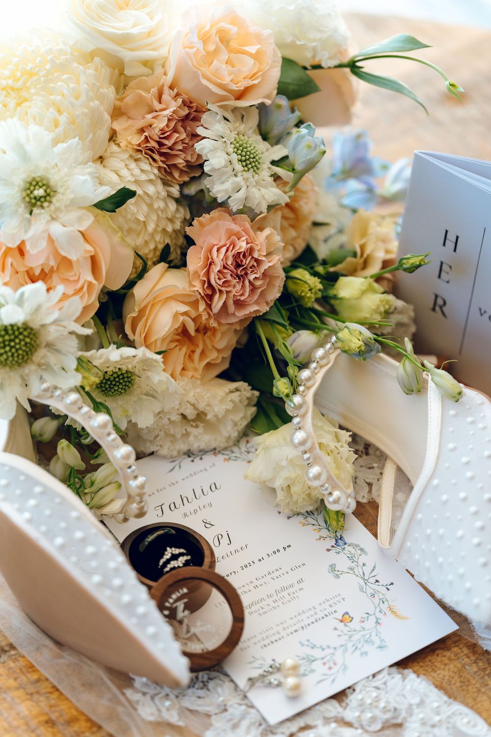 Elegant floral arrangement with peach and white flowers atop wedding stationery and ring box.