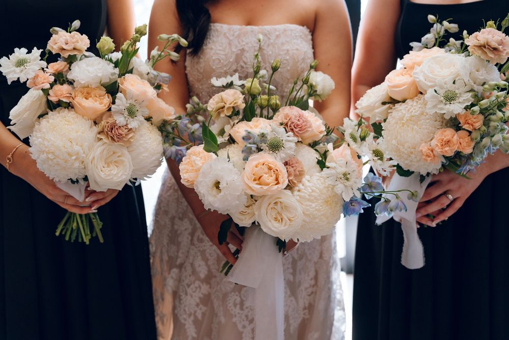 Three wedding bouquets featuring peach roses and white flowers held against dark background.