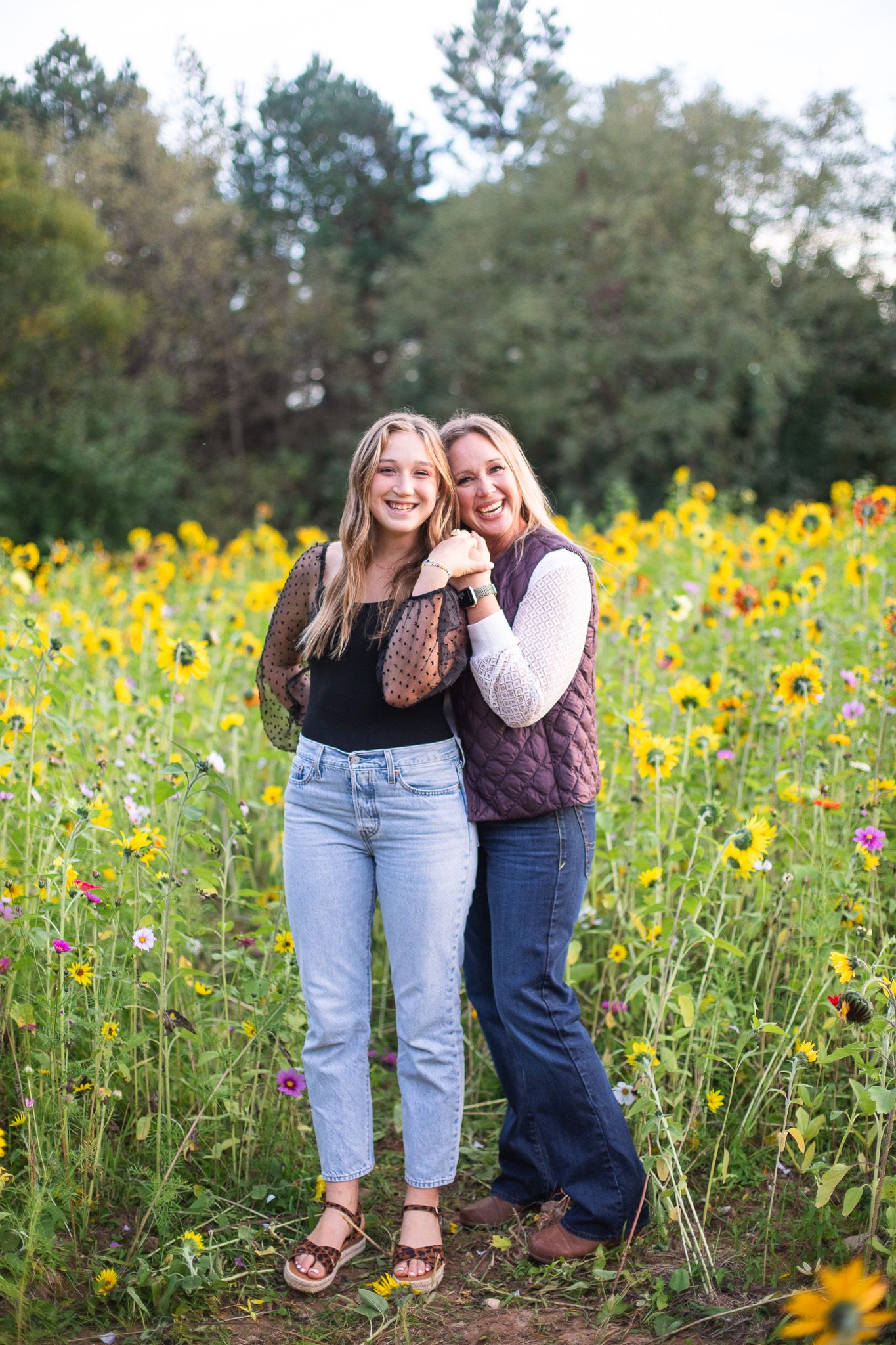 Mom and Daughter stand together in a blooming sunflower field sharing laughter at NCMA