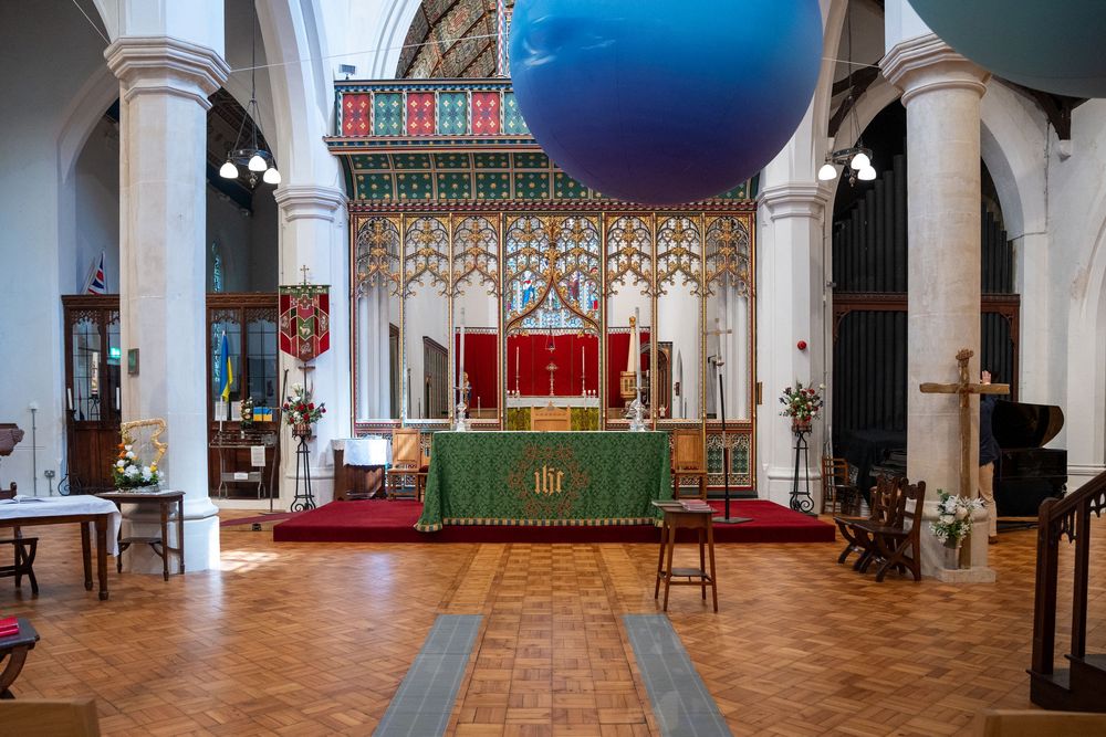 Large open art gallery interior with arched windows and brick flooring displaying contemporary art installations and sculptures.