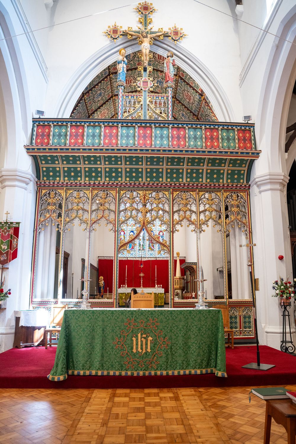 Ornate rood screen with gold cross and green altar cloth in a Gothic church interior featuring vaulted arches and parquet floor.