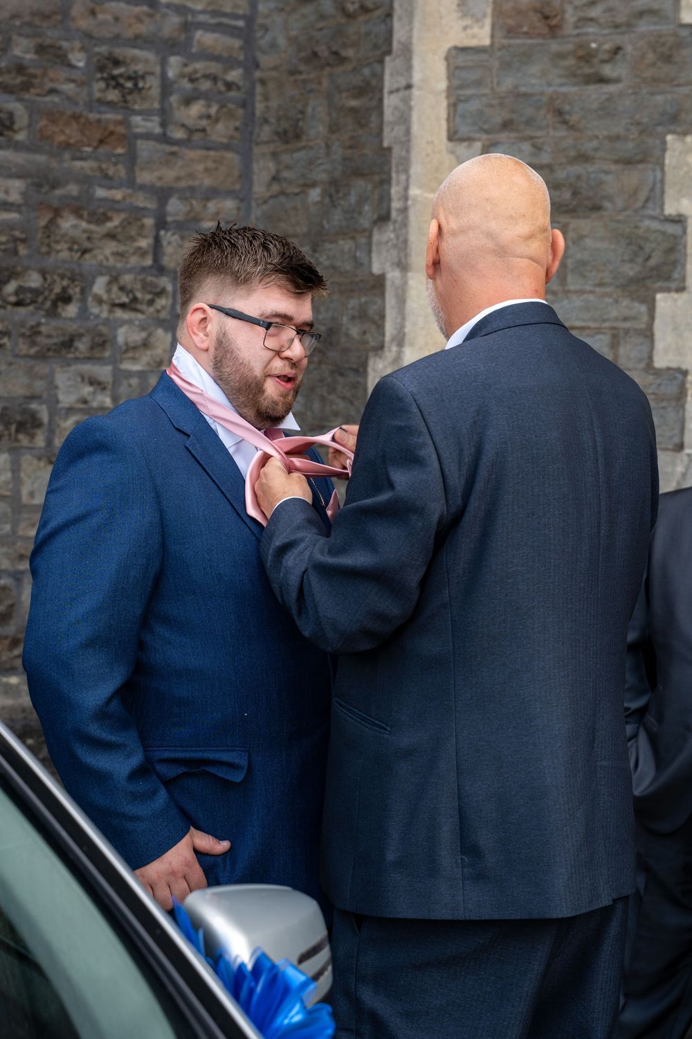 Sequence of photos showing two men in suits talking near a stone wall before getting into a car.