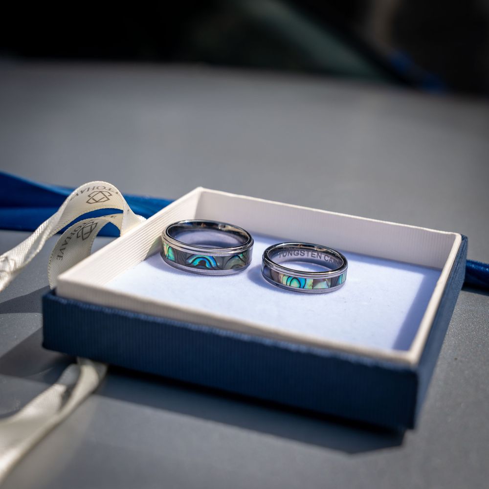 Two matching iridescent titanium wedding rings with colorful patterns displayed in a white box against a blue surface.