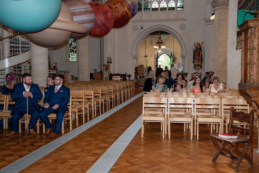 Interior of a church during a wedding ceremony with large colorful balloons and rows of wooden pews.