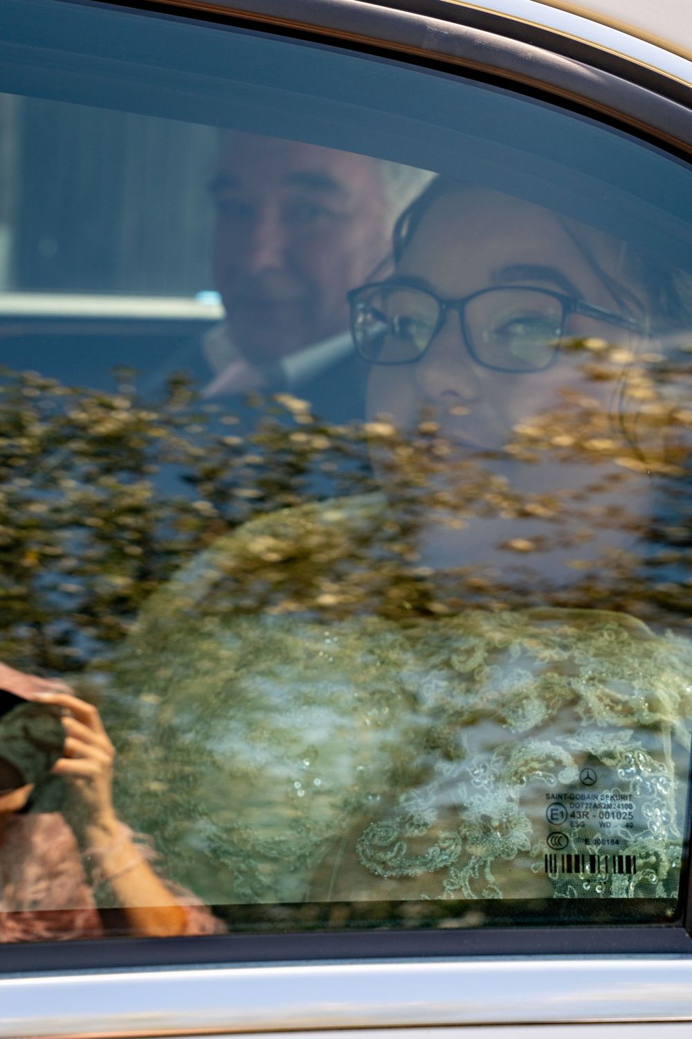 Car window reflection shows blurred trees and scenery on a sunny day.