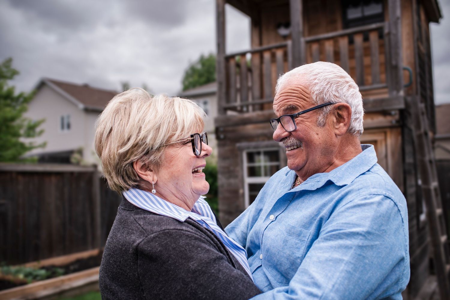 A couple shares a tender moment together in their backyard on a cloudy day.