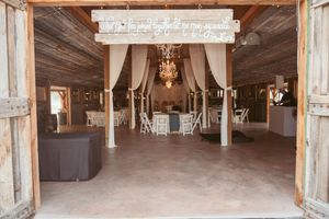 Rustic barn wedding venue interior with elegant white drapes, chandeliers and wooden beams.