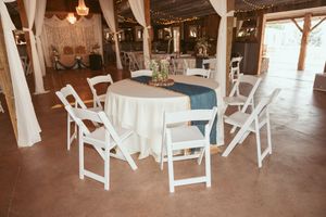White folding chairs arranged around a round table with white linens in a rustic wedding reception venue.