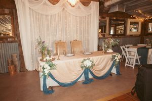 Elegant wedding venue space with white drapes, chandeliers, and rustic wooden beams creating a romantic atmosphere.