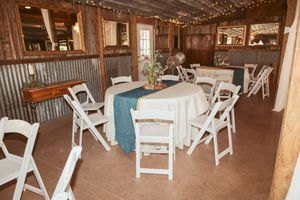 A rustic barn wedding reception venue with wooden beams, string lights and white folding chairs arranged in rows.