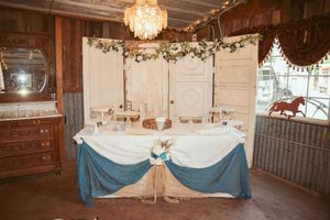 Elegant wedding dessert or cake table decorated with white linens, blue skirting and crystal chandelier in rustic barn venue.