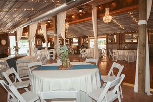 Vintage-style reception hall with round tables, white linens, and crystal chandeliers under wooden beams.