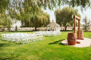 Wedding venue with rows of white chairs facing a wooden barrel altar under weeping willow trees.