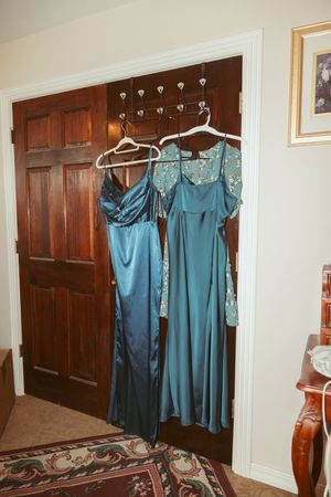 Multiple formal blue dresses hanging on garment racks against a wood-paneled wall in a room with patterned carpet.