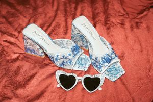 Blue and white floral heels with heart-shaped sunglasses displayed on red fabric.