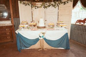 Indoor barn reception area decorated with white draping, floral arrangements, and teal table accents.
