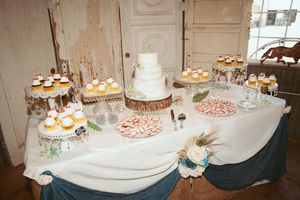 Wedding dessert table with white tiered cake and cupcakes on elegant blue and white tablecloth.