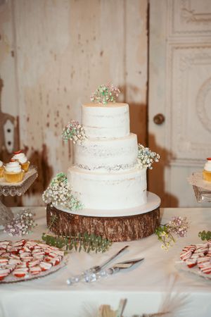Multiple white wedding cakes displayed on wooden slices with delicate floral accents on a white tablecloth.