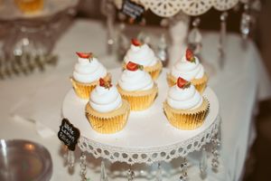 Vanilla cupcakes with white frosting and strawberry toppings displayed on an ornate white cake stand.