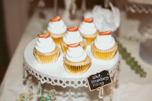 White frosted cupcakes with orange accents displayed on delicate lace cake stand.