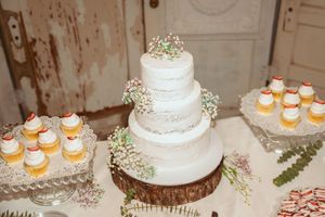 Four-tier white wedding cake decorated with baby's breath on wooden stand.