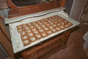 Multiple rows of chocolate chip cookies cooling on marble countertops in a rustic kitchen setting.