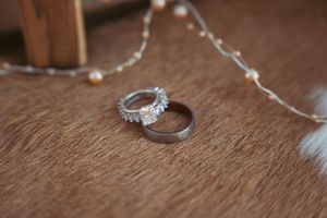 Two wedding rings, one diamond engagement ring and one plain band, resting on a brown textured surface with string decor.