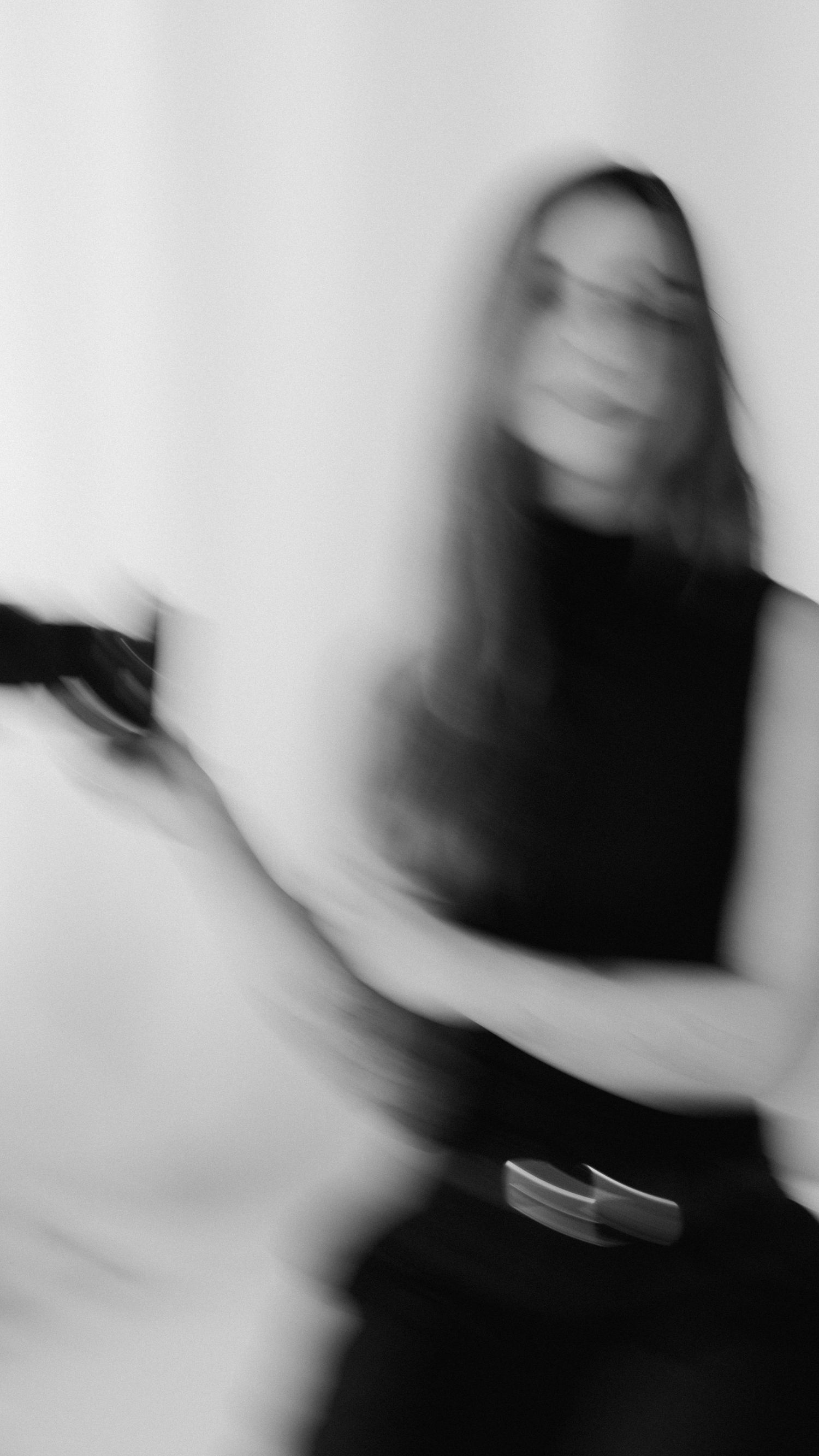Alina streckt die Arme und ihre Kamera nach oben und lächelt dabei, lebendige schwarzweiß-Aufnahme