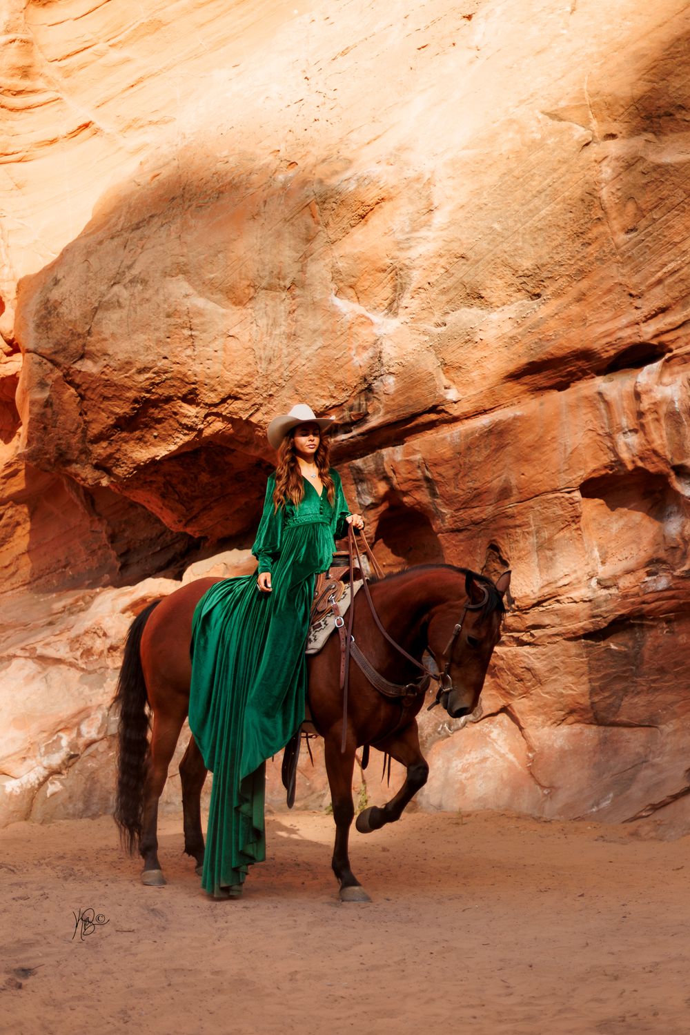 A rider in an emerald dress sits atop a horse against red rock canyon walls.